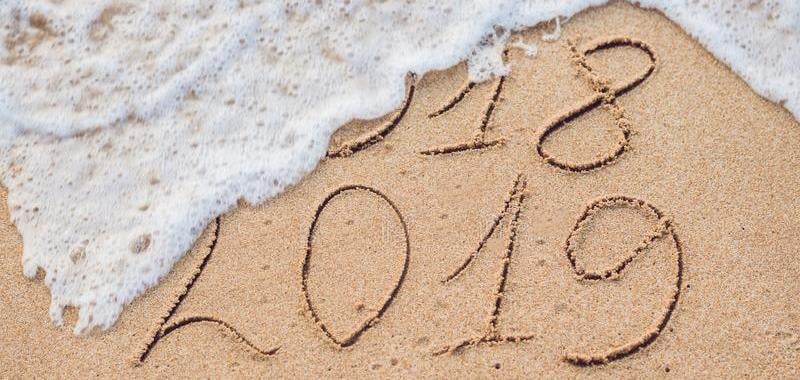 The year numbers 2018 and 2019 written in sand on a beach, 2018 being washed away by sea wave