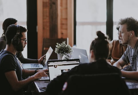 five people sitting around a table and working on laptops