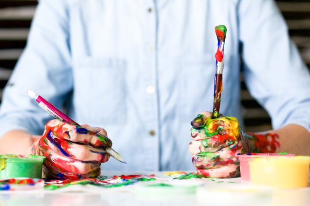 man in a blue shirt paining with his hands covered in paint