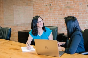 two woman working together with a computer open