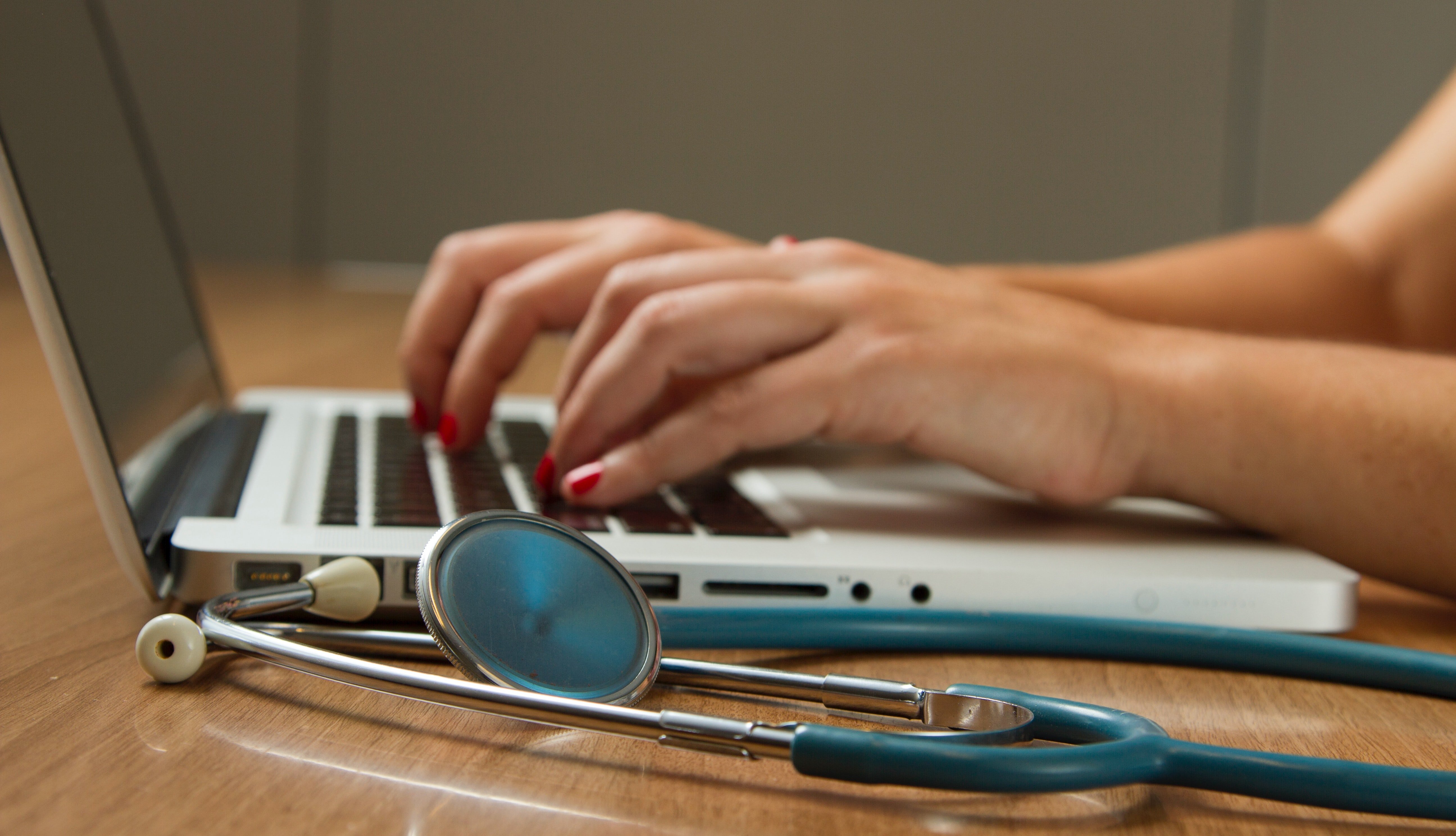 woman typing on a laptop with stethoscope on desk