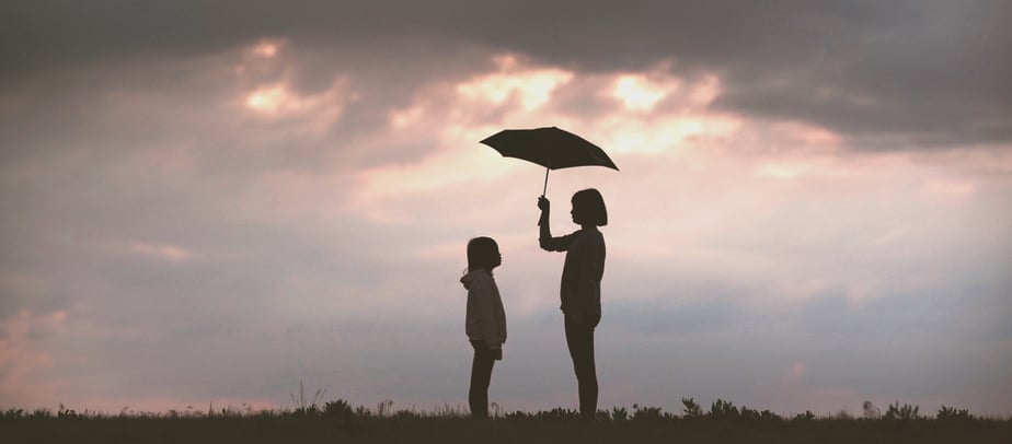 silhouettes of two young girls standing in a field the taller one holding an umbrella with cloudy sunset in the background